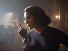 Midge Maisel in a poorly lit club, holding a cigarette and leaning into an old-timey mic. by the Forward
			