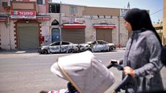 An Arab Israeli woman looks on May 11, 2021 at burnt cars in the central Israeli city of Lod, near Tel Aviv. by the Forward
			
