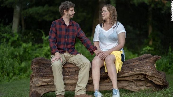 Amy Schumer and Michael Cera in "Life and Beth." They sit on a log and Cer'as hand is on Schumer's leg; Schumer is soaking wet.