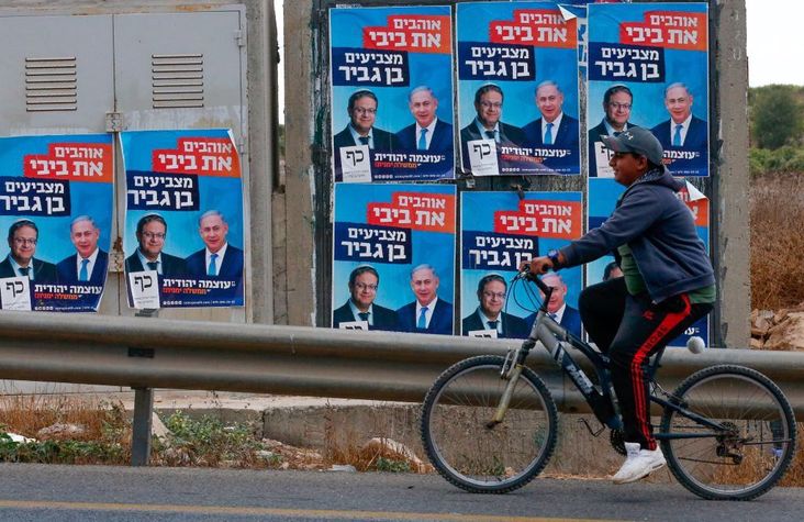 Cyclist rides past campaign posters in the West Bank.