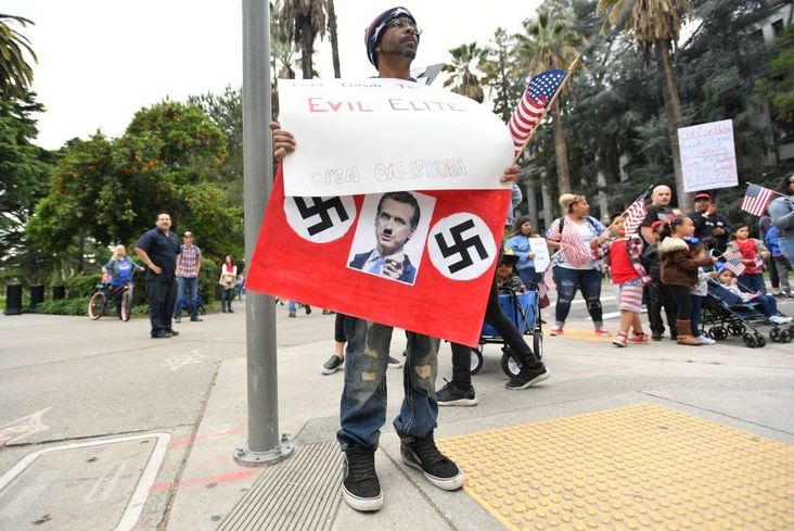 A man displays a sign depicting California Governor Gavin Newsom as a Nazi as hundreds of people gather to protest the lockdown in spite of shelter-in-place rules still being in effect at California's state capitol building in Sacramento, California on April 20, 2020.
