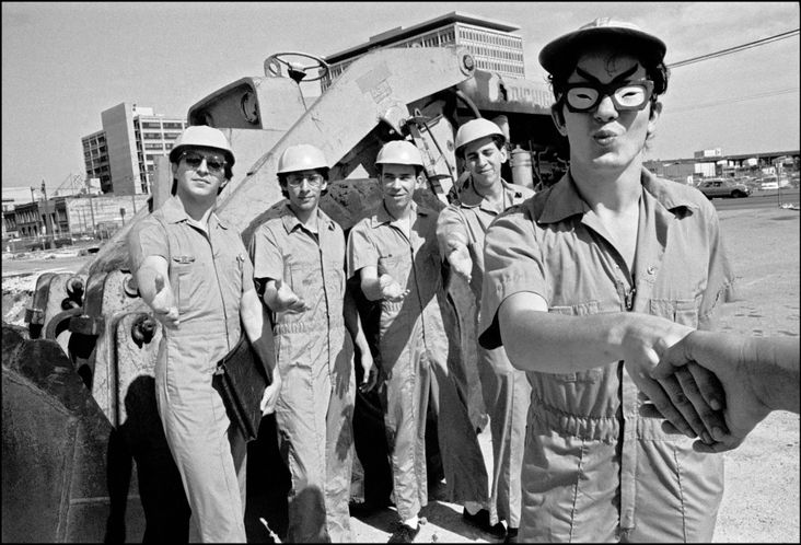 The original Devo lineup, clad in hardhats, poses by a construction site.