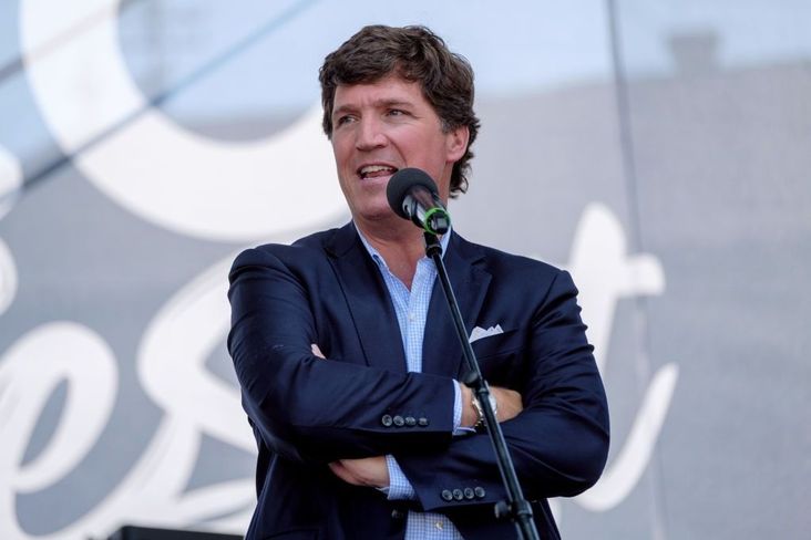 Tucker Carlson speaks at a conservative festival in Hungary in 2021. He is wearing a navy sport coat, no tie, and his arms are crossed as he speaks into a microphone.