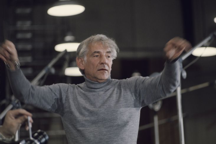 Leonard Bernstein, circa 1974, wearing a gray turtleneck and conducting an orchestra.