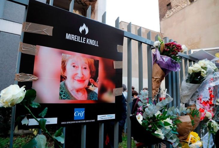 A photograph of Mireille Knoll and flowers are placed on the fence surrounding her building in Paris.