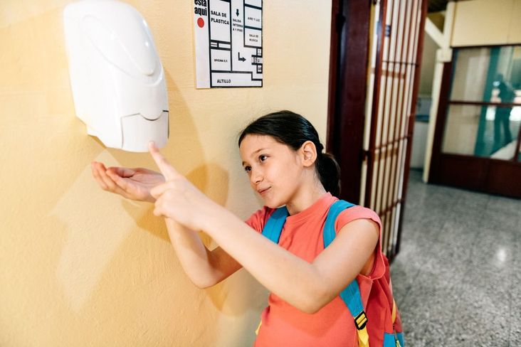 Girl uses hand sanitizer station.