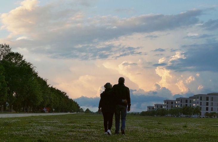 couple walking on field by apartment buildings.