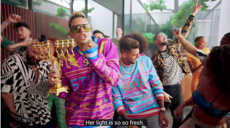 Static and Ben El, helpfully labeled in their sweaters, wearing large sunglasses and gold chains, dance with a gold hanukkiah and a large crowd of backup dancers.