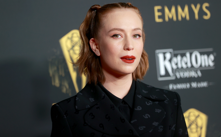 Hannah Einbinder at the Emmys, hair half up in two pigtails, wearing a black suit jacket with an embossed number print.
